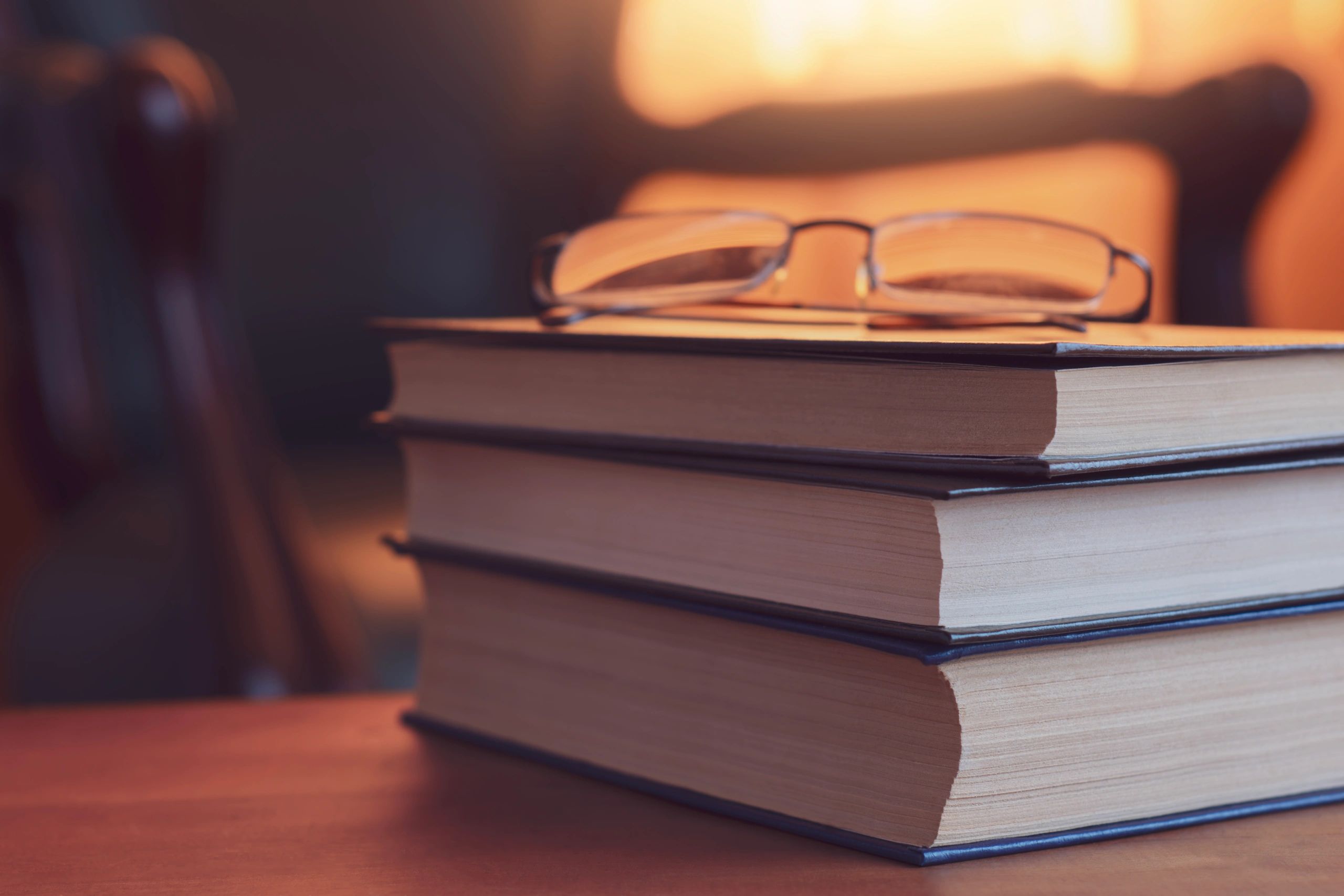 Cozy reading atmosphere with stack of books and eyeglasses on wooden table in warm evening light
